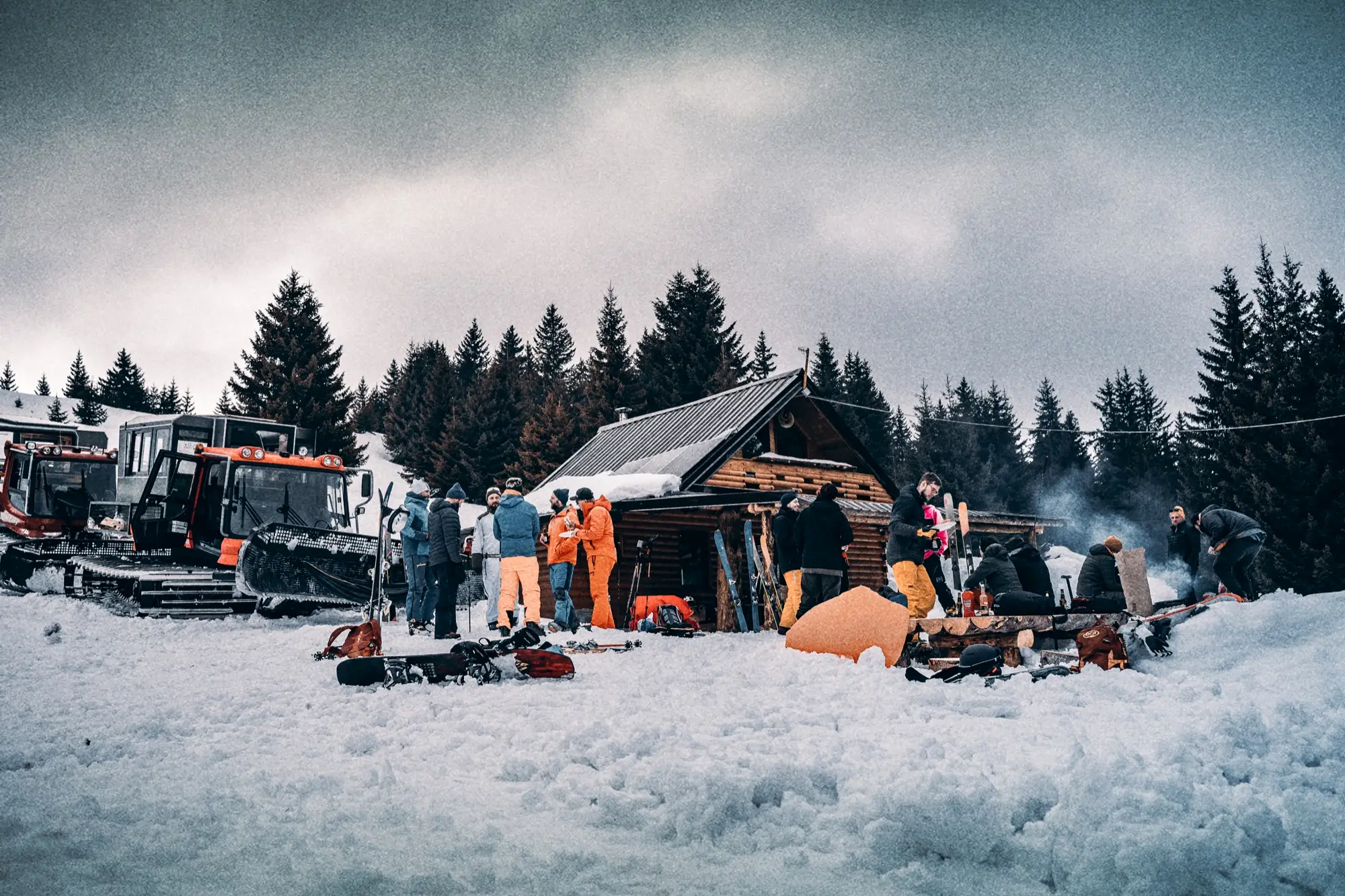 Berghut met snowcats, mensen en rook onder een dreigende lucht